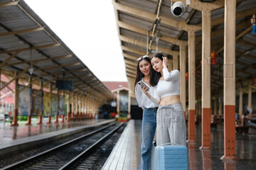 Two women standing at a train station with their luggage