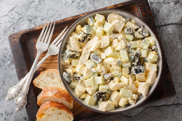 Chicken cream salad with prunes, cucumber and eggs close-up in a bowl on the table. Horizontal top view from above