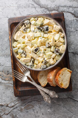Salad with chicken, prunes, boiled eggs and fresh cucumber dressed with mayonnaise close-up in a bowl on a wooden board. Vertical top view from above