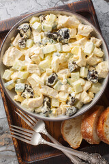 Winter chicken prune salad with boiled eggs and fresh cucumber seasoned with mayonnaise close-up in a bowl on a wooden board. Vertical top view from above