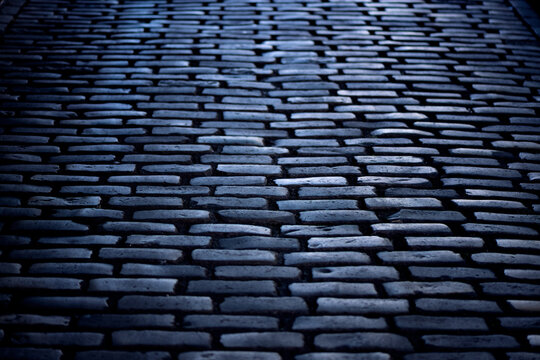Cobblestone street on &ldquo;Montmartre Place du Tertre &ldquo;in Paris, France. Dark historic basalt blocks reflecting blue sky in a shady area. Old pavement pattern background with typical surface and structure