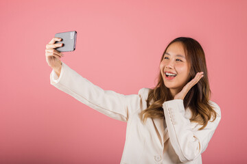 Happy Asian portrait beautiful cute young woman smiling excited making selfie photo, video call on smartphone studio shot isolated on pink background, female hold mobile phone raise hand say hello