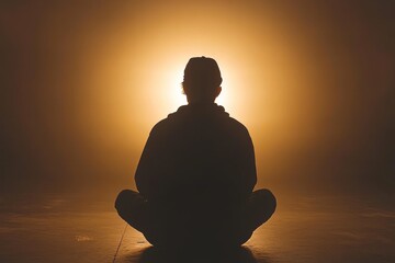 Silhouette of a person meditating in a warm glowing light evoking calm introspection and the peaceful balance of mind and body in a serene setting
