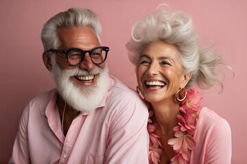 Happy elderly couple smiling in pink outfits on a pink background.