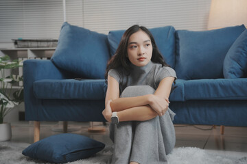 Obraz premium Sad, anxious young woman sits alone on the floor at home, overwhelmed by thoughts and emotions, reflecting on problems and feeling stressed