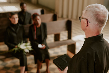 Over shoulder view of silver-haired priest offering up praying and holding Bible