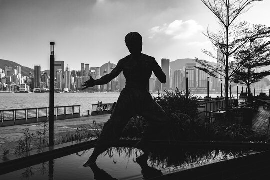 Hong Kong City, Hong Kong - April 15, 2024: Bruce Lee statue stands on the waterfront at Victoria Harbour, Hong Kong, surrounded by the city skyline