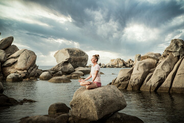 woman meditating on rock on the beach