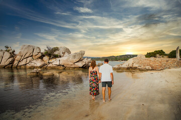couple walking on beautiful beach with rocks at sunset