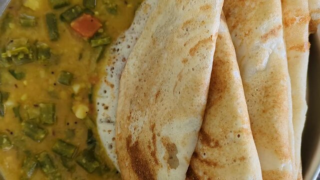 Tracking shot of homemade crispy dosa served with beans and lentils curry at home