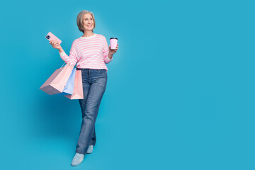 Naklejka premium Full body photo of senior woman shopping bags device coffee look empty space wear trendy striped outfit isolated on blue color background