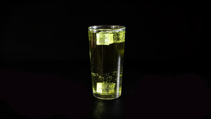Lemonade with Rising Bubbles and Ice Cubes in Glass on a Black Background