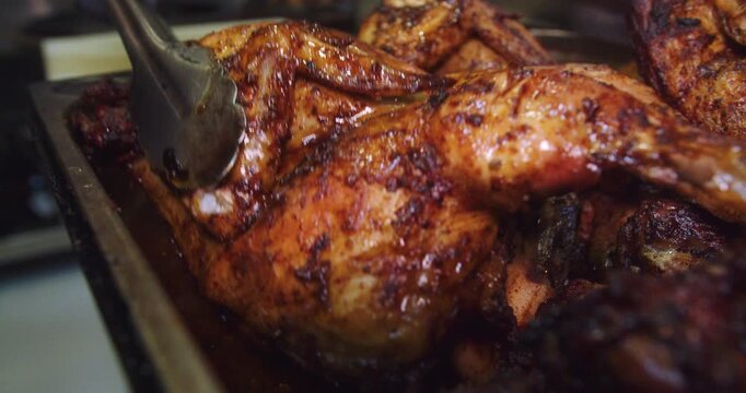 Beautiful slow motion shot of a charcoal roasted chicken being coded and removed with large tongs inside a restaurant kitchen.