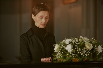 Senior mourning widow touching black coffin as goodbye gesture