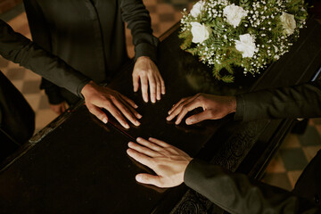 High angle shot of unrecognizable biracial hands on coffin next to bouquet of white roses