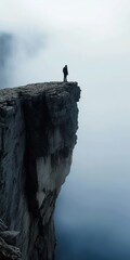 A man stands on a cliff overlooking a body of water. The sky is cloudy and the man is alone