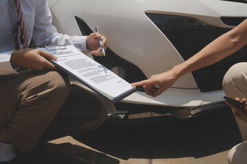 Side view of writing on clipboard while insurance agent examining car after accident