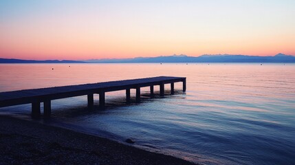 Fototapeta premium A peaceful beach with a small wooden pier extending into the water. The calm, reflective surface of the ocean and the soft light of sunset create a serene and contemplative scene