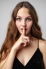 Young Woman With Brown Hair Makes a Silly Face and Holds Her Finger to Her Lip