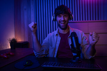 A gamer is actively participating in a live streaming session while speaking into a microphone. The setting features a stylish, dimly lit room with colorful lighting, creating an engaging atmosphere © Grustock