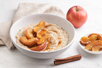 Sweet oatmeal porridge with baked apple slices, cinnamon and caramel sauce in a gray bowl on a light background, top view. Delicious homemade food
