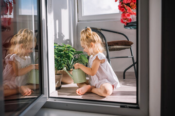 Little girl watering flowers on a sunny balcony in a bright, cheerful home setting
