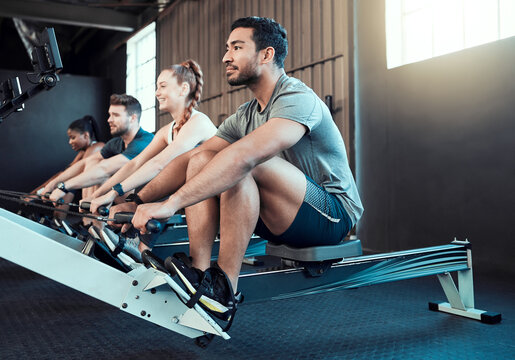 Fitness, class and man on rowing machine for health, wellness and body workout in gym. Exercise, healthy people and strong athlete on ergometer equipment for arms, cardio training and muscle growth