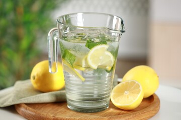 Refreshing lemonade with mint in jug and citrus fruits on table, closeup