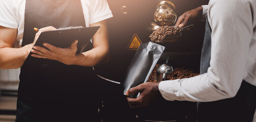 Worker control process packing fresh coffee in bag package at roasting factory.