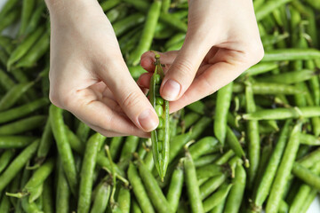 Woman opening fresh green pea pods, top view