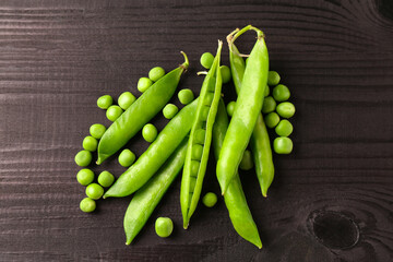 Fresh green peas and pods on black wooden table, top view