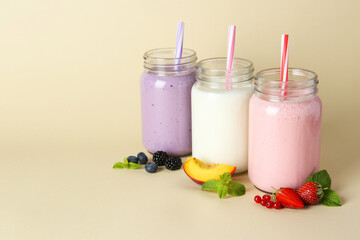 Different tasty yogurts in mason jars, peach, fresh berries and mint on pale yellow background, space for text
