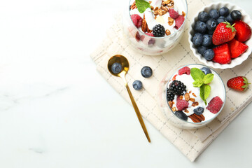 Tasty yogurt with fresh berries, granola and mint in glasses served on white table, flat lay. Space for text