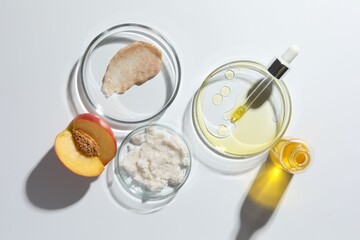Petri dishes with different cosmetic products and peach on white background, flat lay