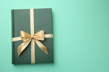 Book tied with golden ribbon on green background, top view with space for text. Perfect gift