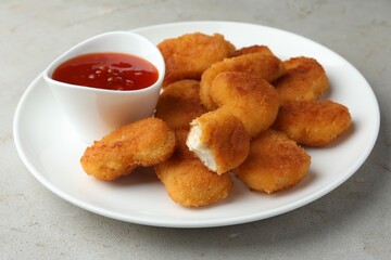 Tasty chicken nuggets with chili sauce on grey textured table