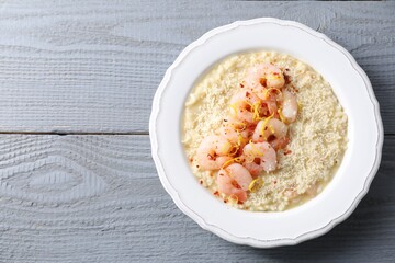 Delicious risotto with shrimps and cheese on grey wooden table, top view. Space for text