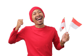 Excited Indonesian man in a red long sleeve T-shirt and beanie holds the Indonesian flag and raises...