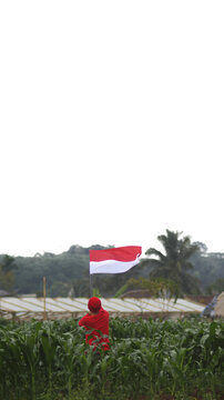Indonesian man wearing a red shirt celebrates Indonesian Independence Day on August 17 by waving the Indonesian red and white flag in the middle of a cornfield.