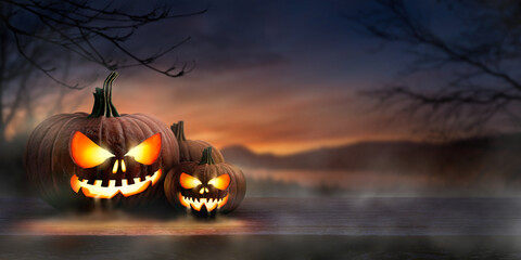 A scary spooky glowing carved halloween pumpkin lantern, Jack O' Lanterns, on the left of a wooden...