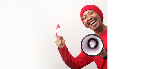Indonesian man in a white T-shirt shouts loudly while holding a megaphone behind a white wall. He is announcing special offers or discounts during Indonesia Independence Day special promotion
