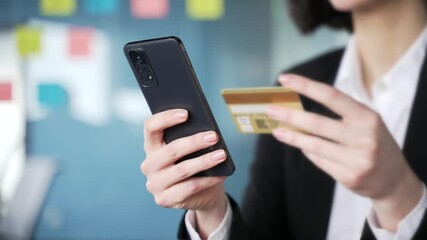 Close up. Female hands holding smartphone and credit card for online shopping or financial transaction in office setting. Professional office worker or businesswoman conducting secure payment