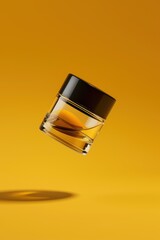A transparent glass jar with a black lid, floating against a vibrant yellow background, showcasing its sleek design.