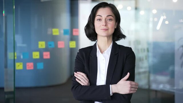 Portrait of confident businesswoman standing in modern office with crossed arms. Headshot of serious young female manager. Professional woman in business attire, representing leadership and success