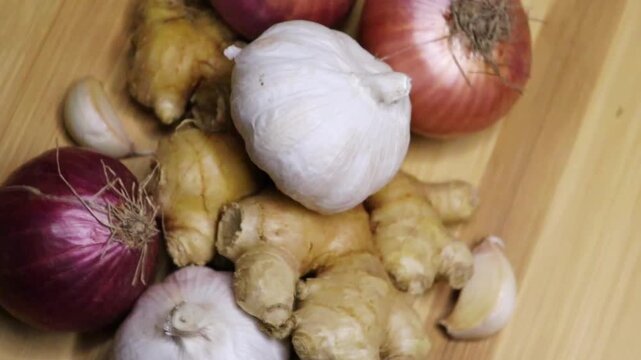 Aerial view of whole raw onion, garlic and ginger rotate on table for cooking. Whole onion, garlic and ginger closeup 4k video. Healthy organic cooking preparation. Chef preparing meal ingredients.