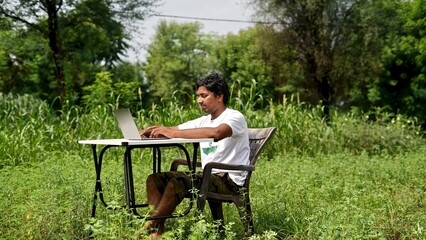 Indian young boy doing work from home. Man sitting on office table at garden doing work on internet