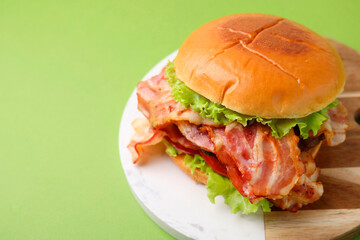 Delicious burger with bacon and lettuce on green background, space for text