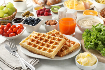 Tasty breakfast. Belgian waffles, orange juice, butter and other food on light wooden table, closeup