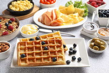 Tasty breakfast. Belgian waffles, blueberries and other food on grey textured table, closeup