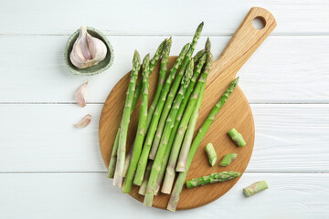 Fresh green asparagus stems and garlic on white wooden table, flat lay